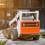 istockphoto-1269840120-612×612 Skid loader stands in front of entrance to new multi-storey house and waits for garbage to be loaded into bucket. Mini bulldozer waiting for cargo in front of porch